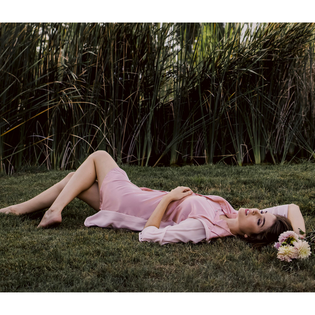  Model wearing pink aliferous shirt dress by inlarkin lying on green grass holding a bouquet of flowers