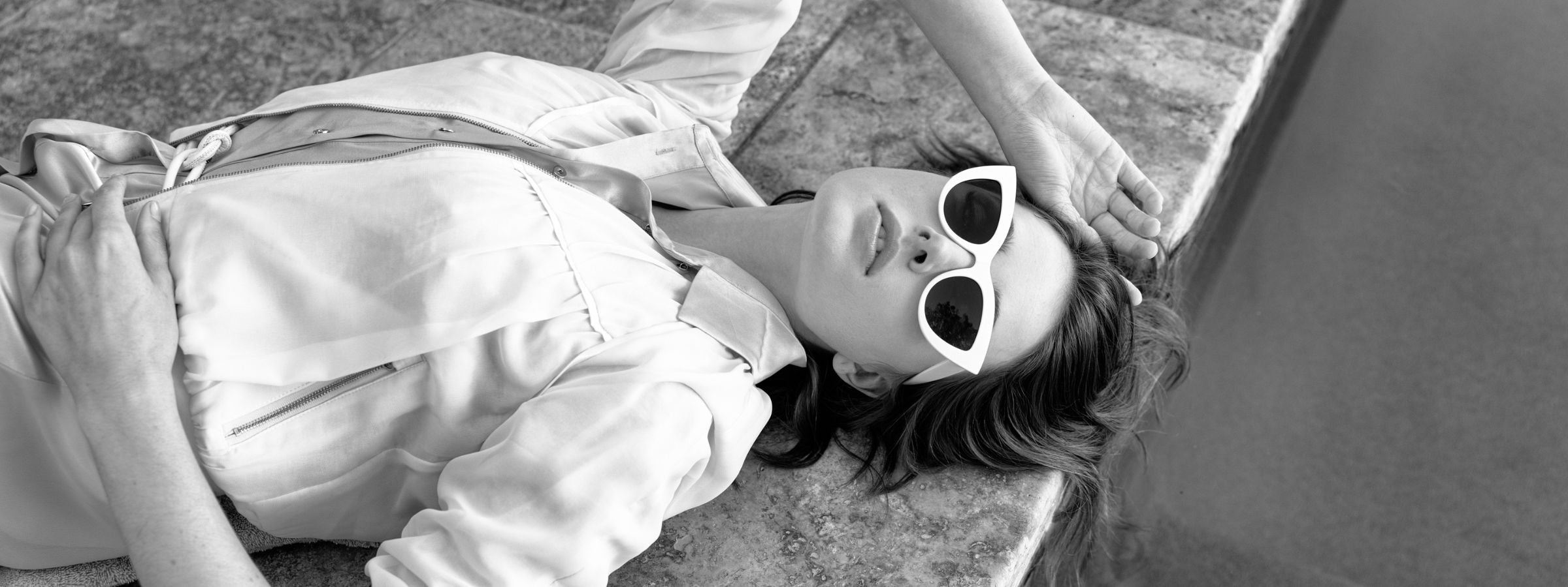 Woman lying at a pools edge with stylish sunglasses on wearing a coral Aliferous dress and signature white beauty bomber jacket by inlarkin showing how comfortable and stylish athglamour can be