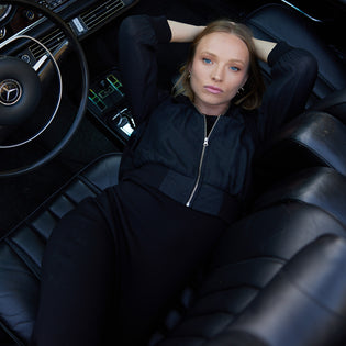  woman lying across the front seats of a vintage convertible mercedes benz wearing a black form fitting dress and a black zip up bomber jacket showing a monochromatic outfit pairing by inlarkin