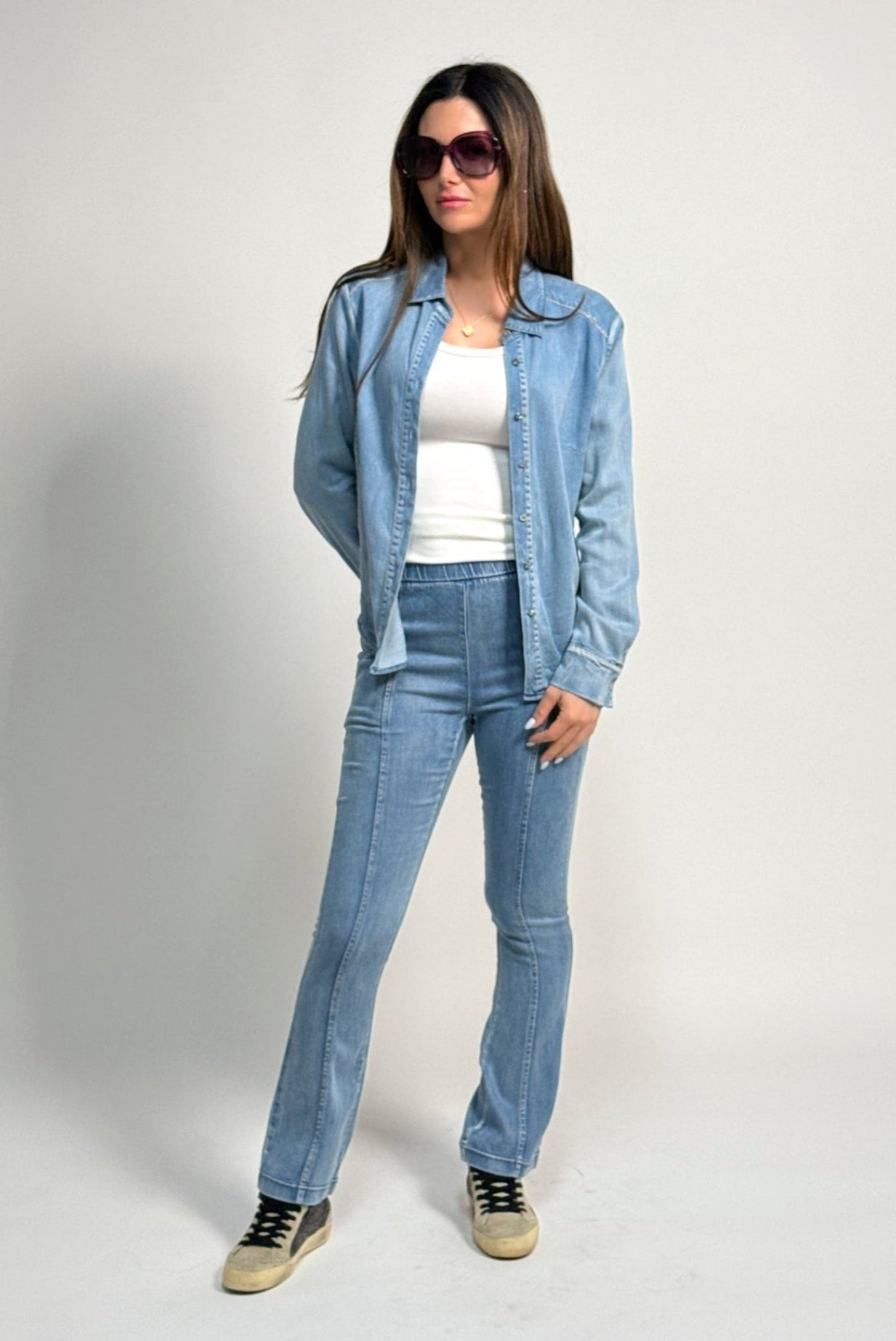 Woman wearing a denim outfit featuring the water jean by inlarkin with sunglasses on a plain background