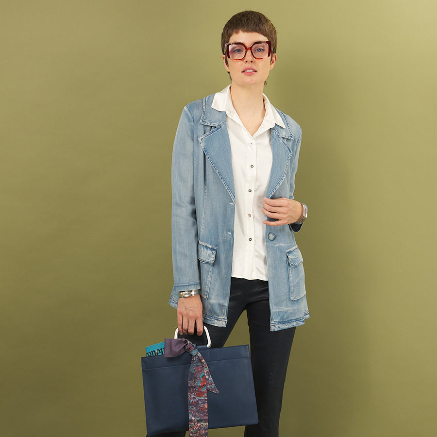 Woman holding a blue bag with a patterned tie wearing a white aliferous shirt and jane jacket by inlarkin against a green background