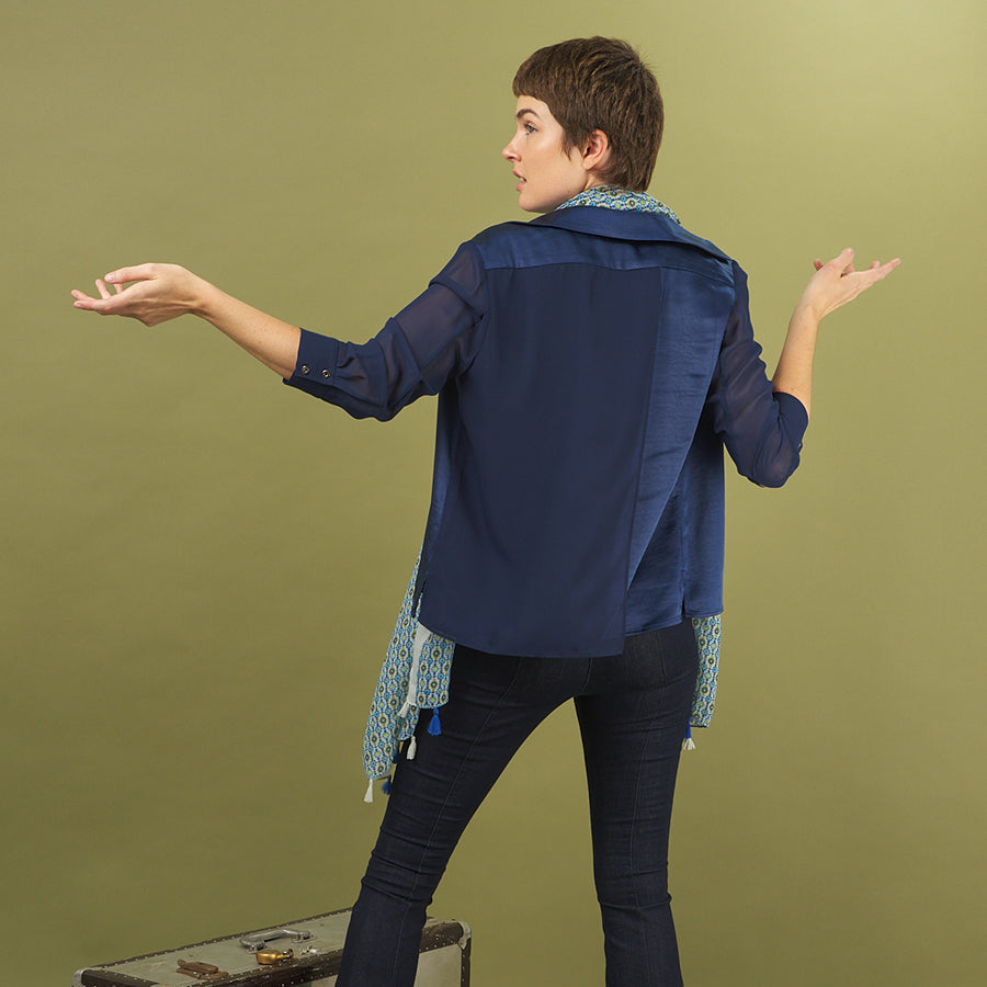 Woman in a navy aliferous shirt by inlarkin standing with arms outstretched on a green background with a piece of luggage