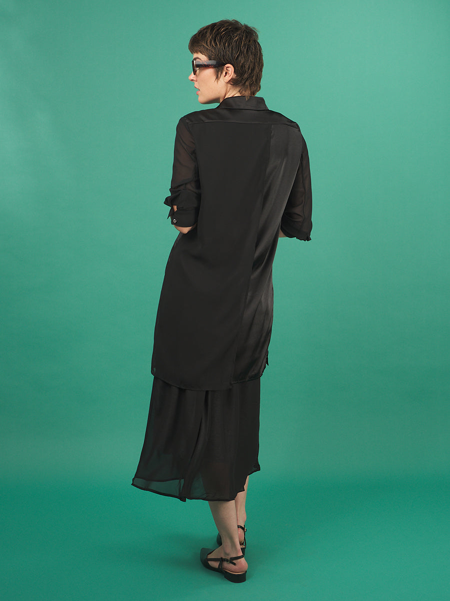 woman wearing a black aliferous shirtdress by inlarkin against a green background, view from the back