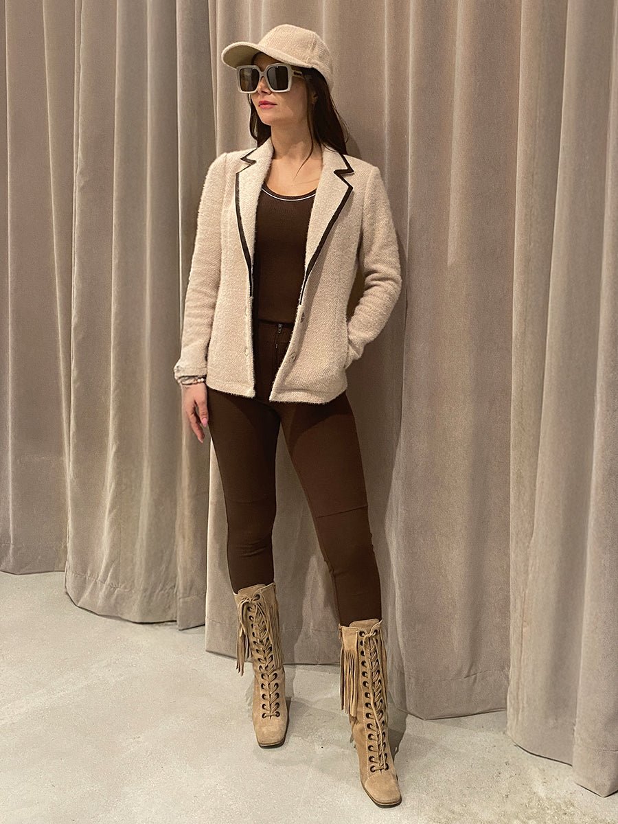Woman wearing an austin coat in oat, and brown zippie leggings by inlarkin, and beige boots against a plain background