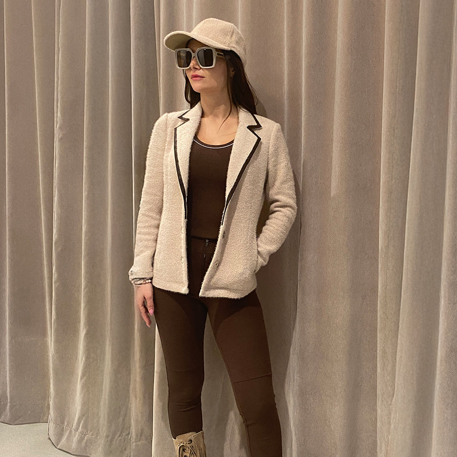 Woman wearing an austin coat in oat, and brown zippie leggings by inlarkin, and beige boots against a plain background