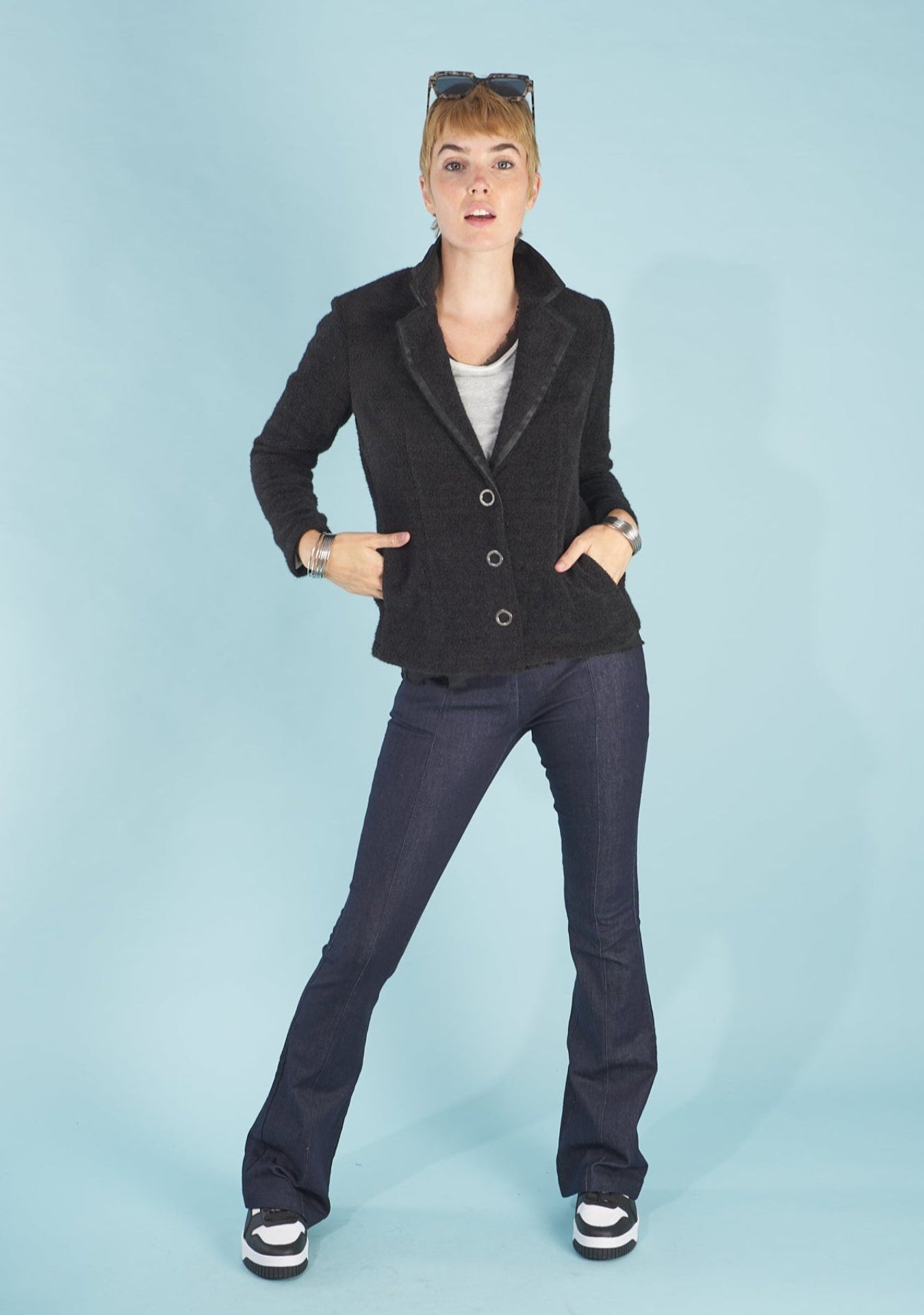 Woman wearing a black austin blazer by inlarkin and sublime jeans against a light blue background