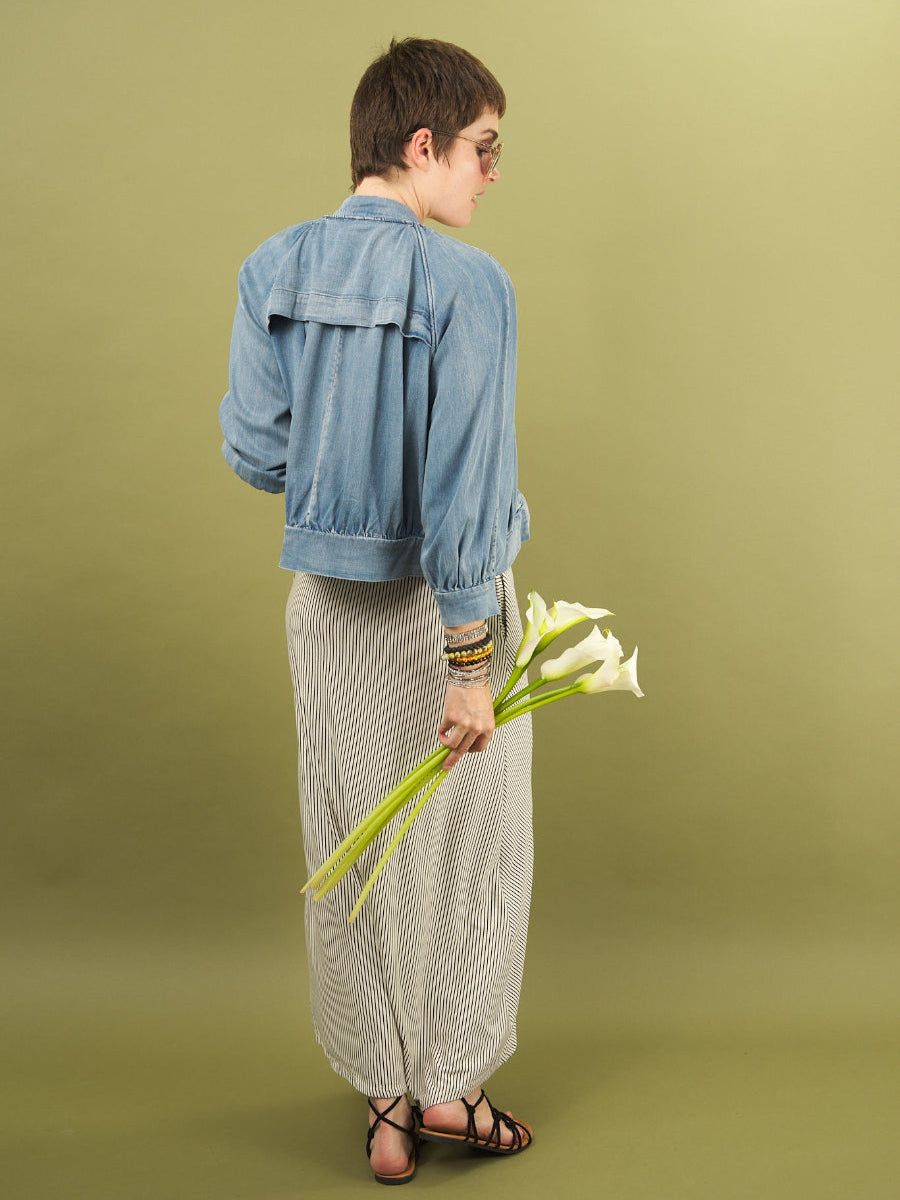 Woman wearing a denim boy bomber jacket by inlarkin holding white flowers against a green background