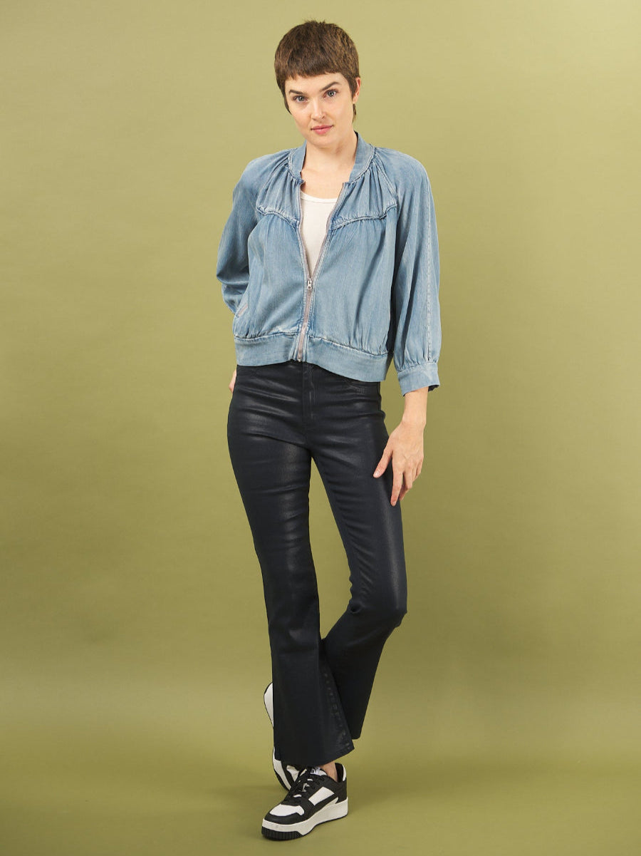 woman wearing a denim boy bomber jacket by inlarkin and bootleg pants on a green background