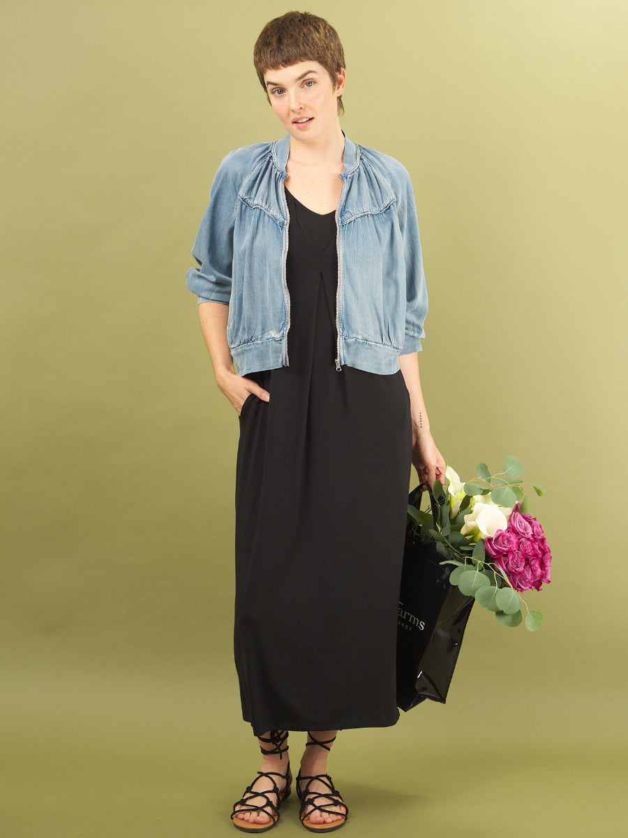 Woman in a black dress and denim jacket holding flowers against a green background