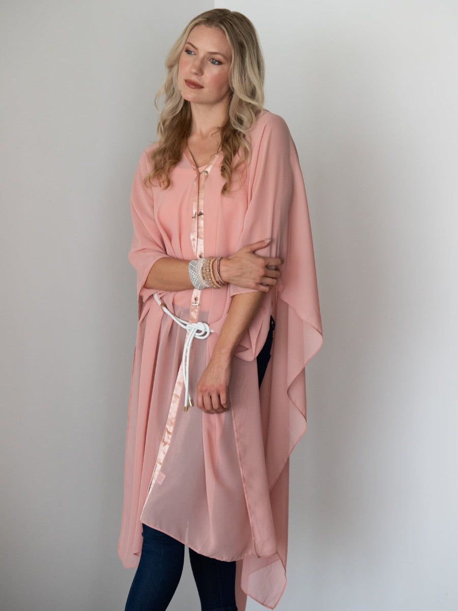 Woman wearing a coral colored kimono-style dottie coverall by inlarkin against a plain background