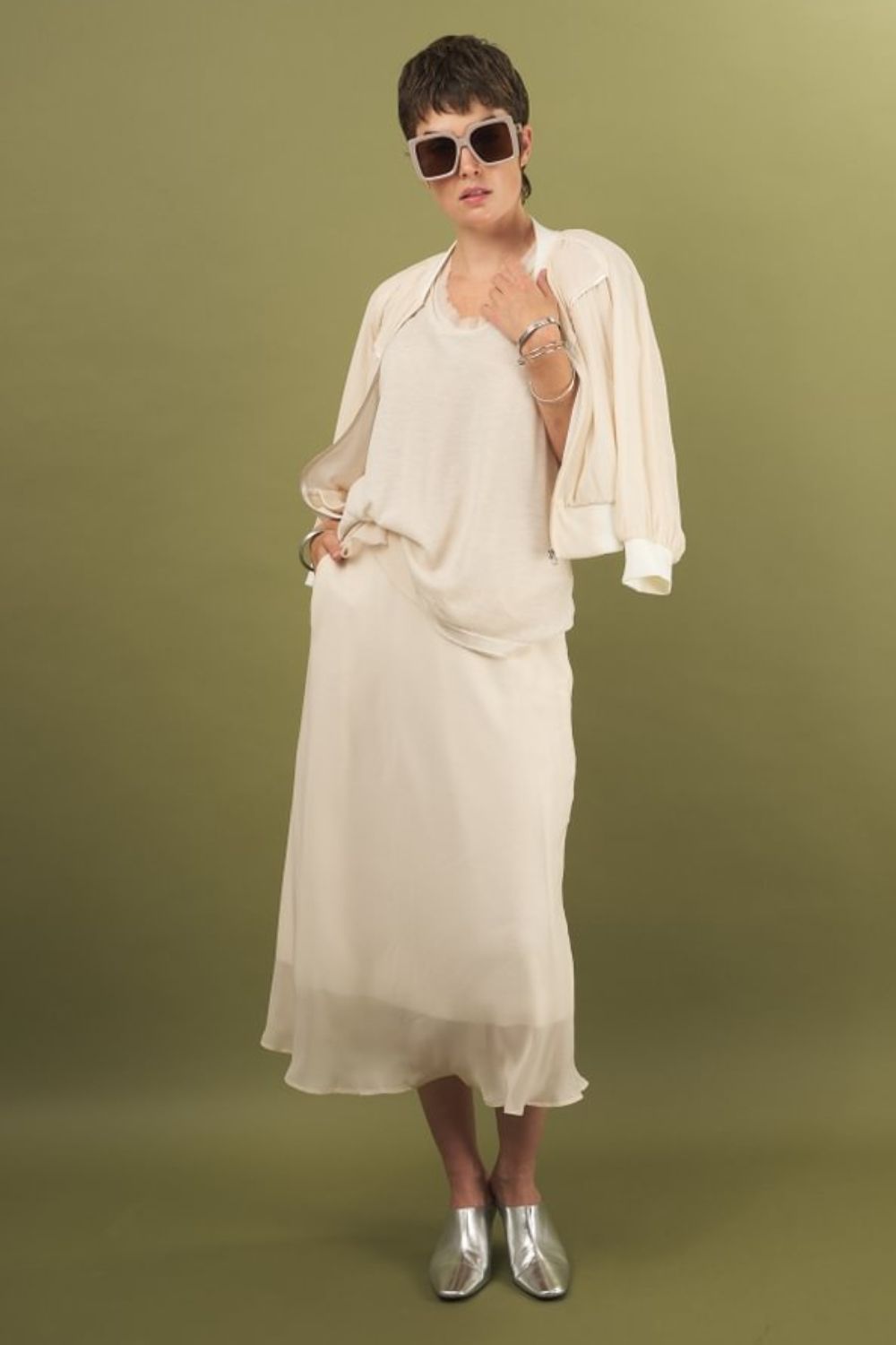 woman wearing the glasswing shell 2.0 in cream paired with the slay skirt in cream and beauty bomber jacket in cream by inlarkin against a green backdrop