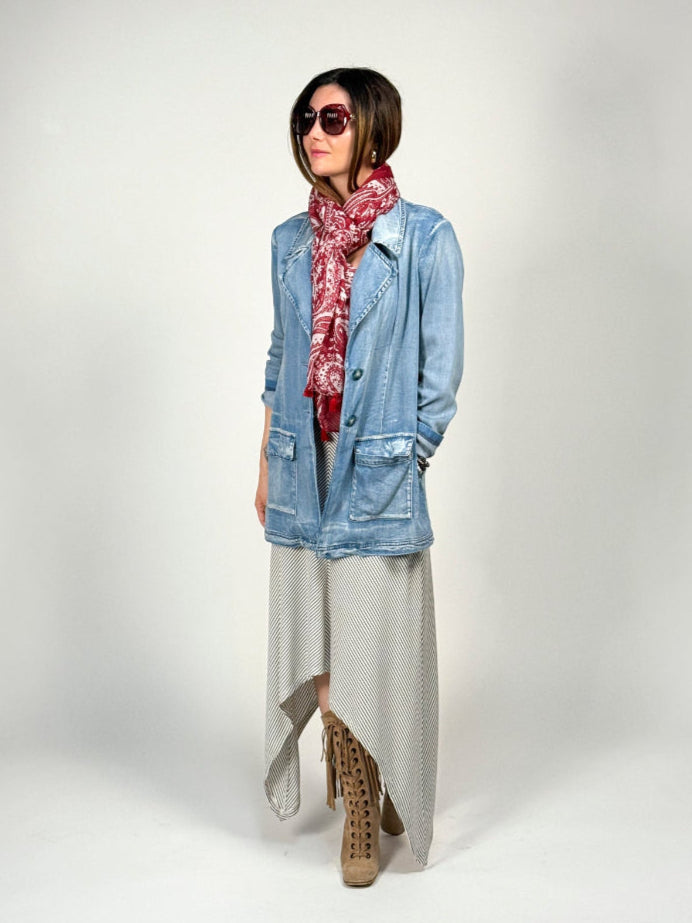 Person wearing a light blue denim jacket, gray dress, and patterned scarf on a white background