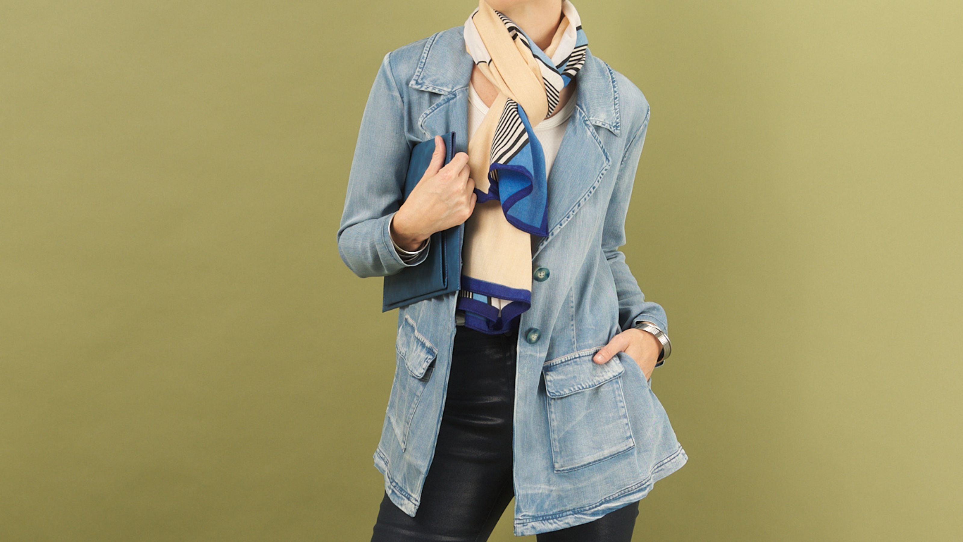 Woman wearing a denim jane jacket by inlarkin with a scarf on an olive green background
