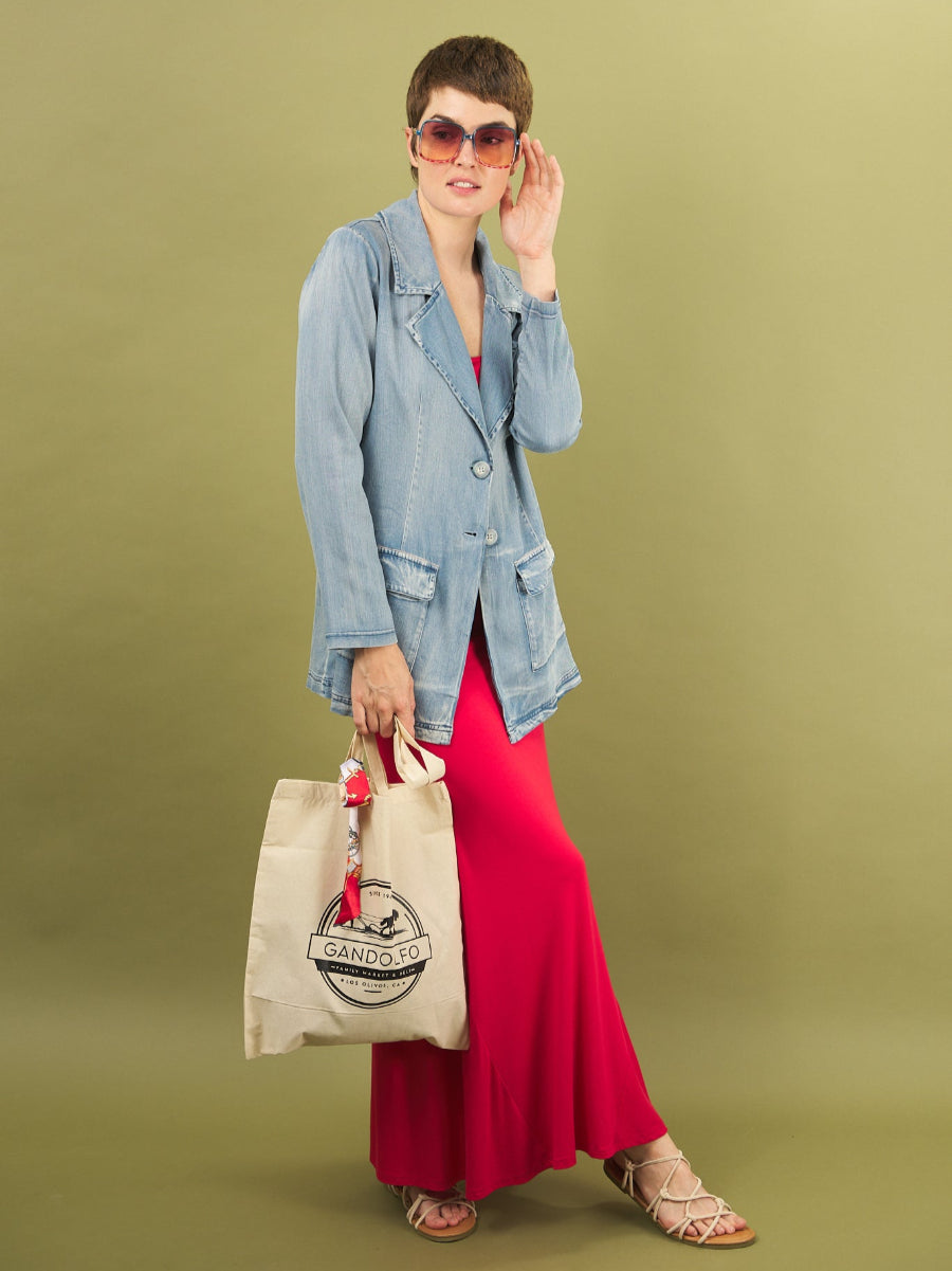 Woman in a denim jacket and red dress holding a beige tote bag against a green background