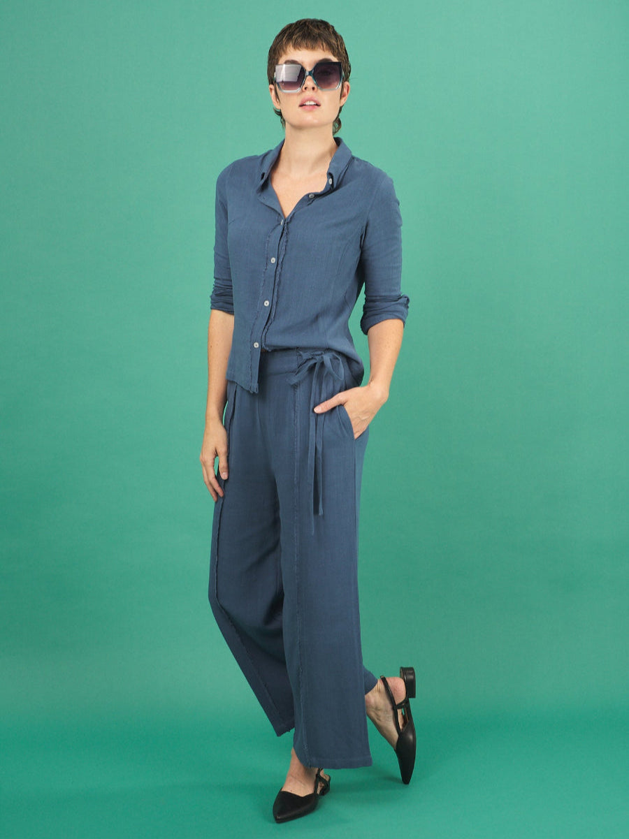Woman wearing a french blue linen fray shirt and pant by inlarkin against a green background