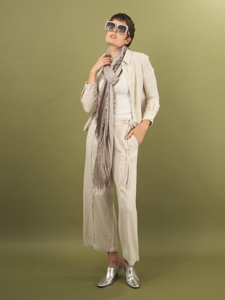 Woman in a sand linen fray shirt and pant by inlarkin with sunglasses and a scarf on a green background