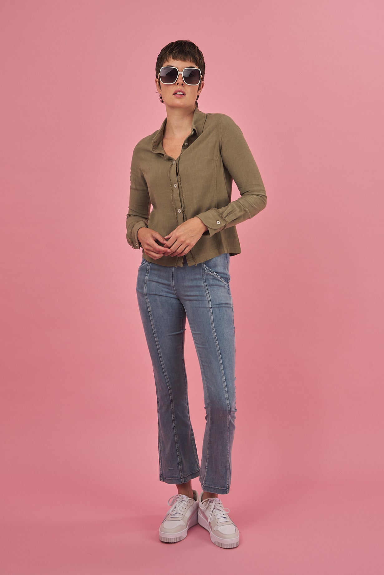 woman wearing a green sage linen shirt and denim water jean by inlarkin on a pink background