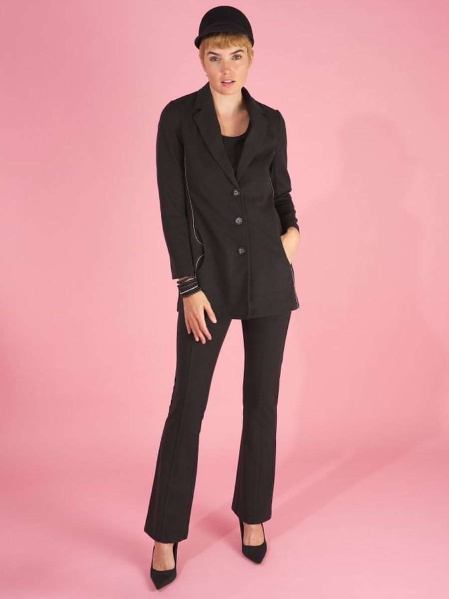 Woman wearing a black maxine blazer by inlarkin and a black cap on a pink background