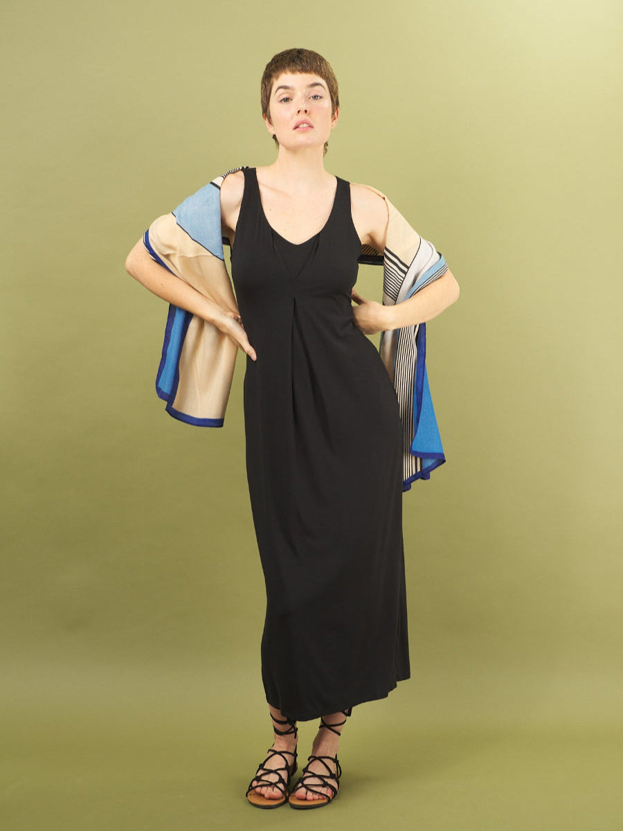 Woman wearing a black royal tuck dress by inlarkin holding a colorful scarf against a green background