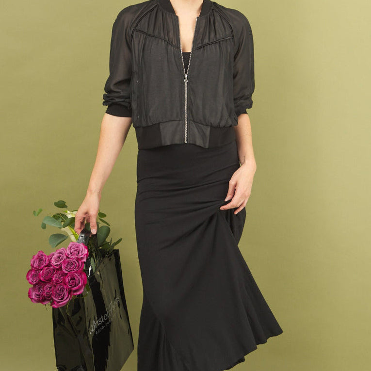 Woman in black sharyn dress and beauty bomber by inlarkin holding flowers against a green background