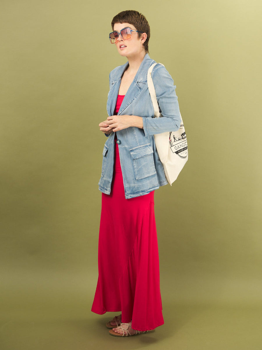 Woman wearing a red sharyn dress by inalrkin and denim boy bomber jacket with a white bag on a green background