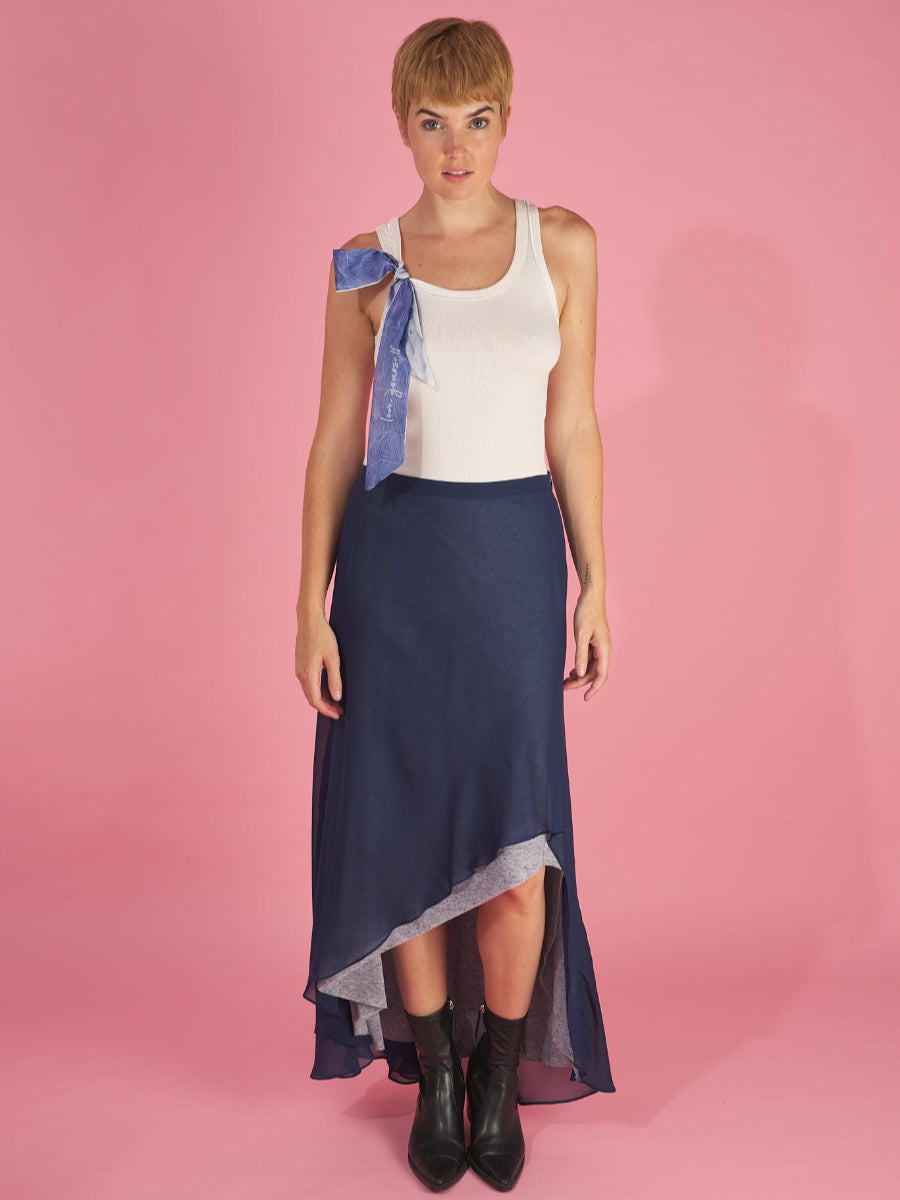 Woman wearing a white top and navy blue shay skirt by inlarkin with a pink background