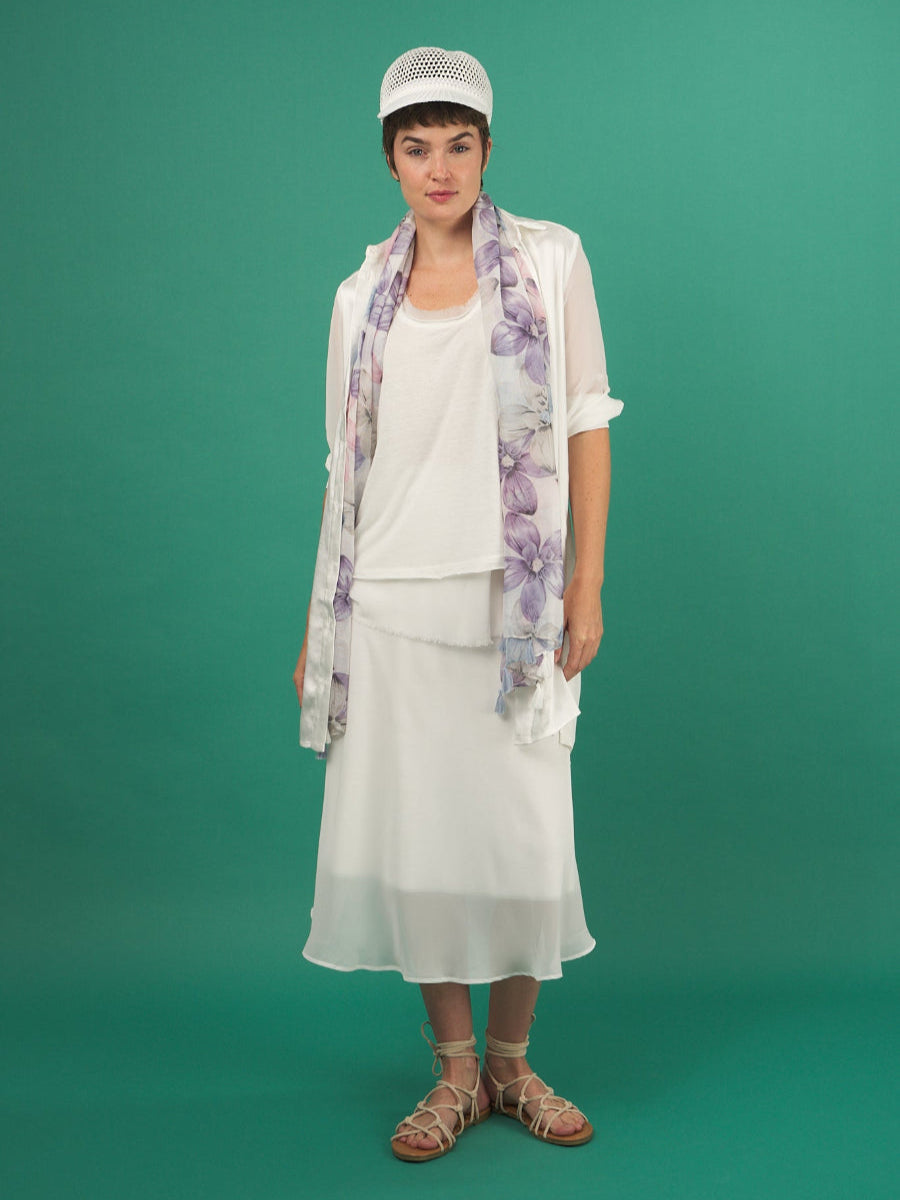 Woman wearing a white slay skirt by inlarkin outfit with a floral scarf against a green background