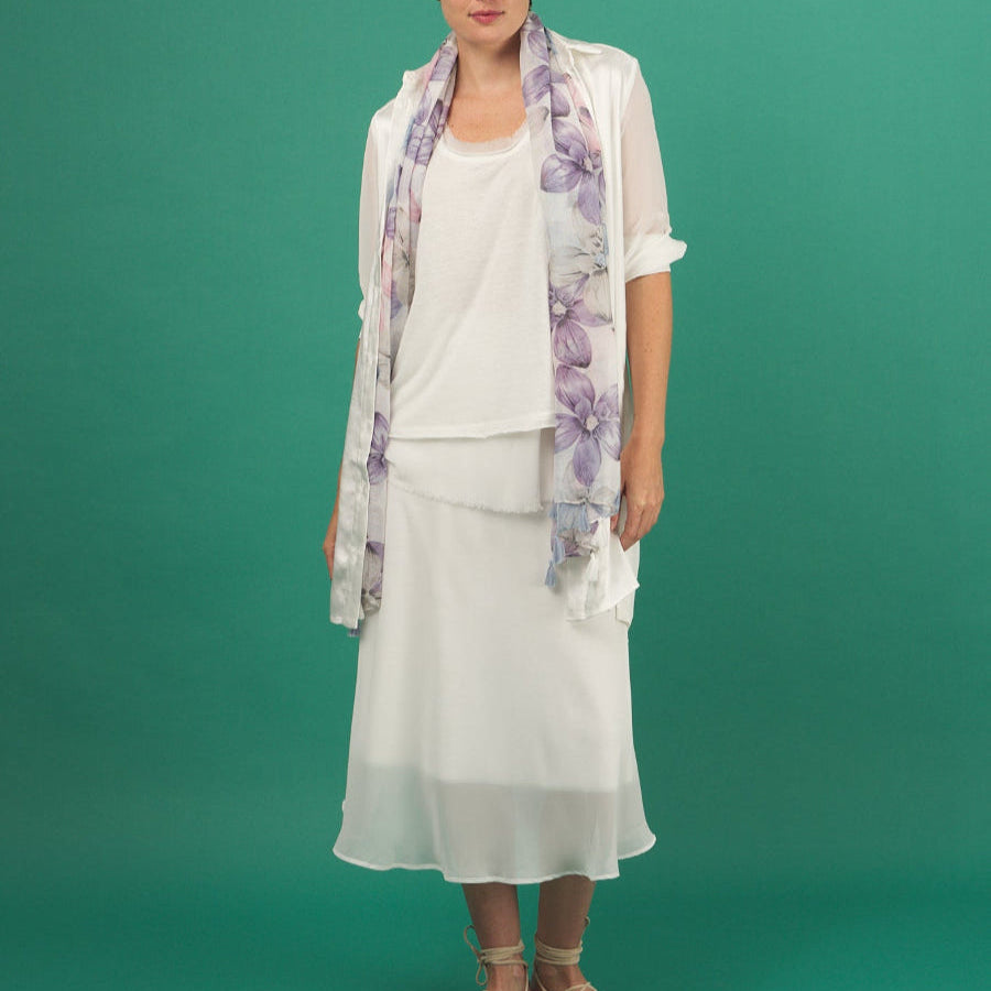 Woman wearing a white slay skirt by inlarkin outfit with a floral scarf against a green background