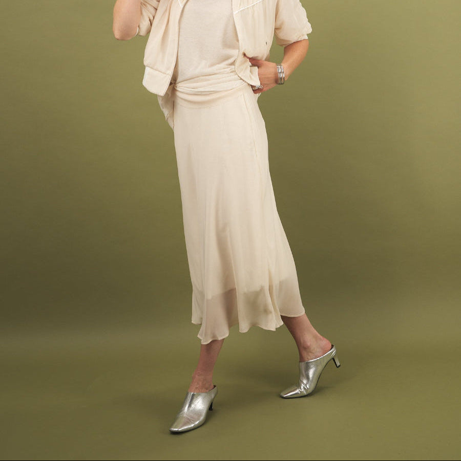 Woman in a cream slay skirt and beauty bomber jacket outfit by inlarkin with sunglasses on a green background