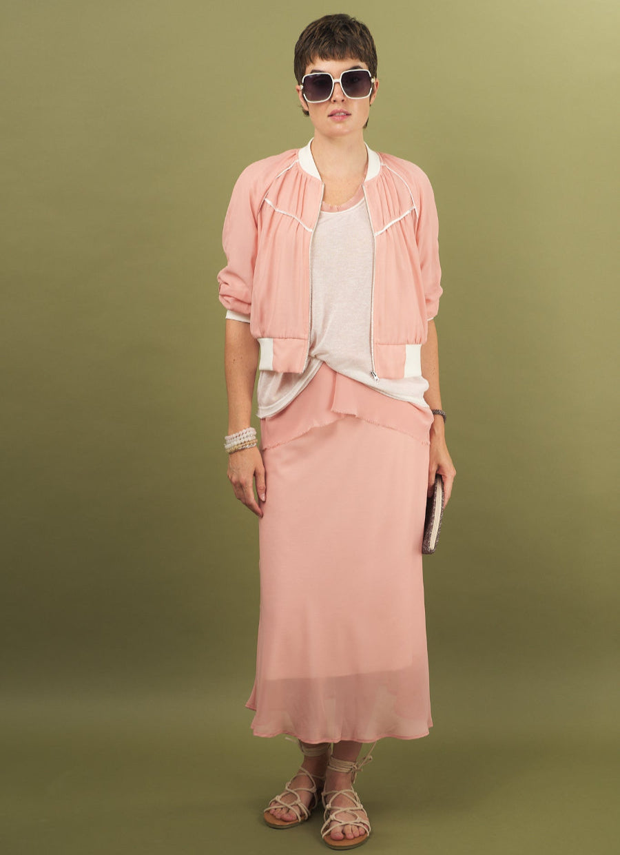 Woman wearing a coral slay skirt and beauty bomber jacket outfit by inlarkin with sunglasses on a green background