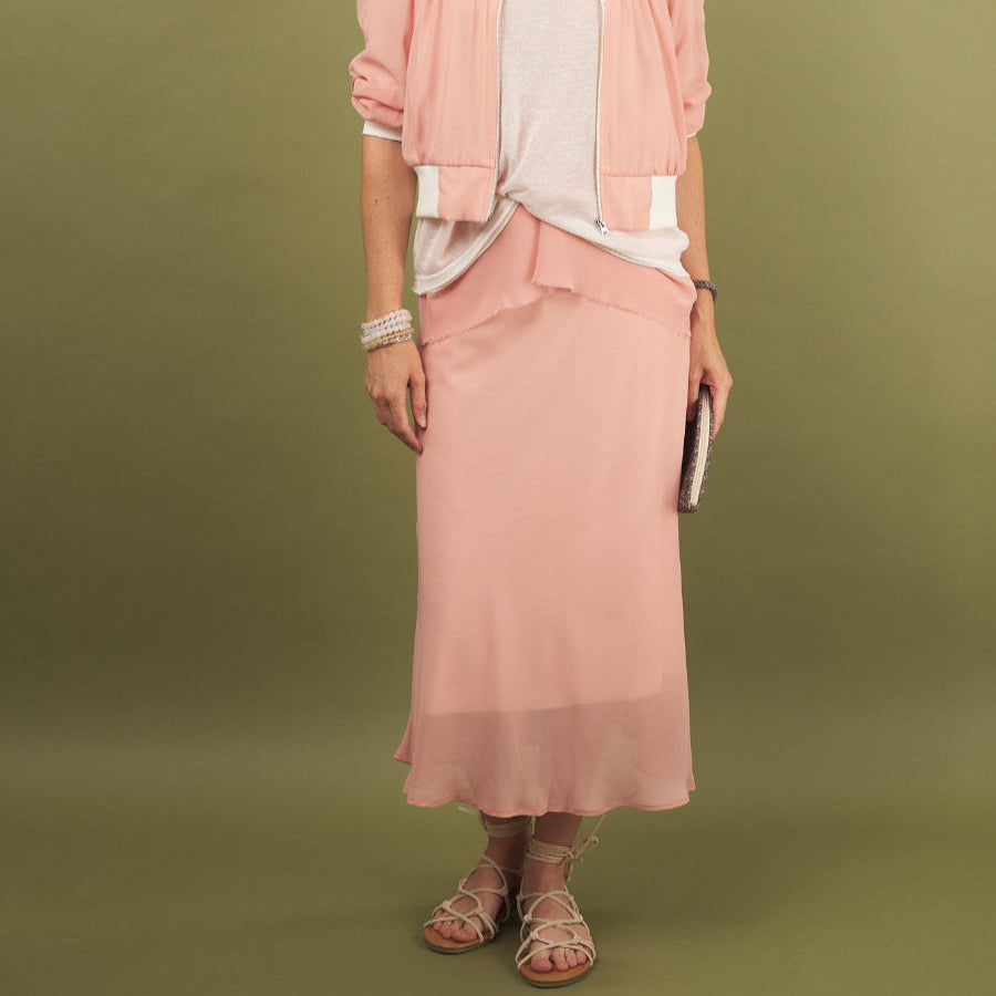 Woman wearing a coral slay skirt and beauty bomber jacket outfit by inlarkin with sunglasses on a green background