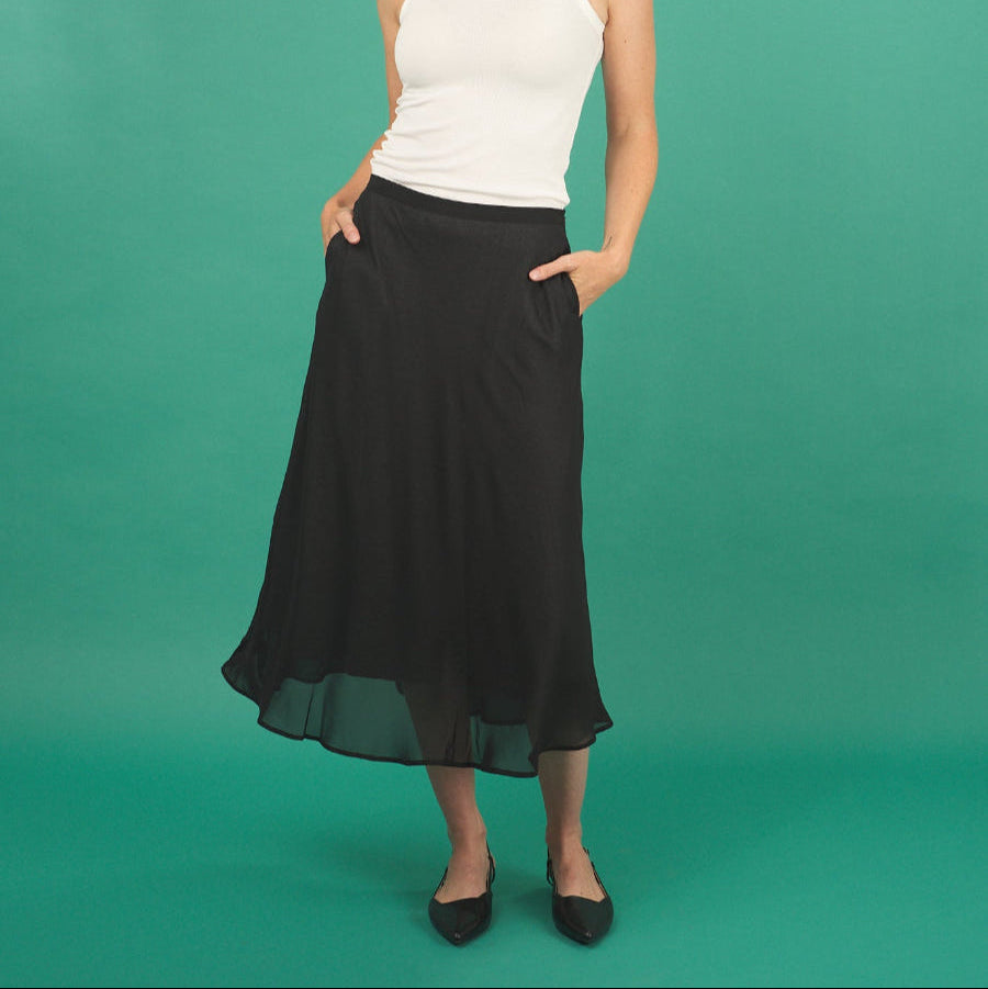 Woman wearing a white tank top and black slay skirt by inlarkin against a green background