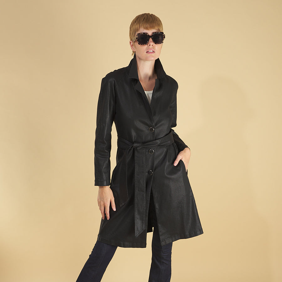 the toni trench coat by inlarkin in black front view showing the high gloss fabric, collar, side seam pockets and belt, paired with the sublime jean