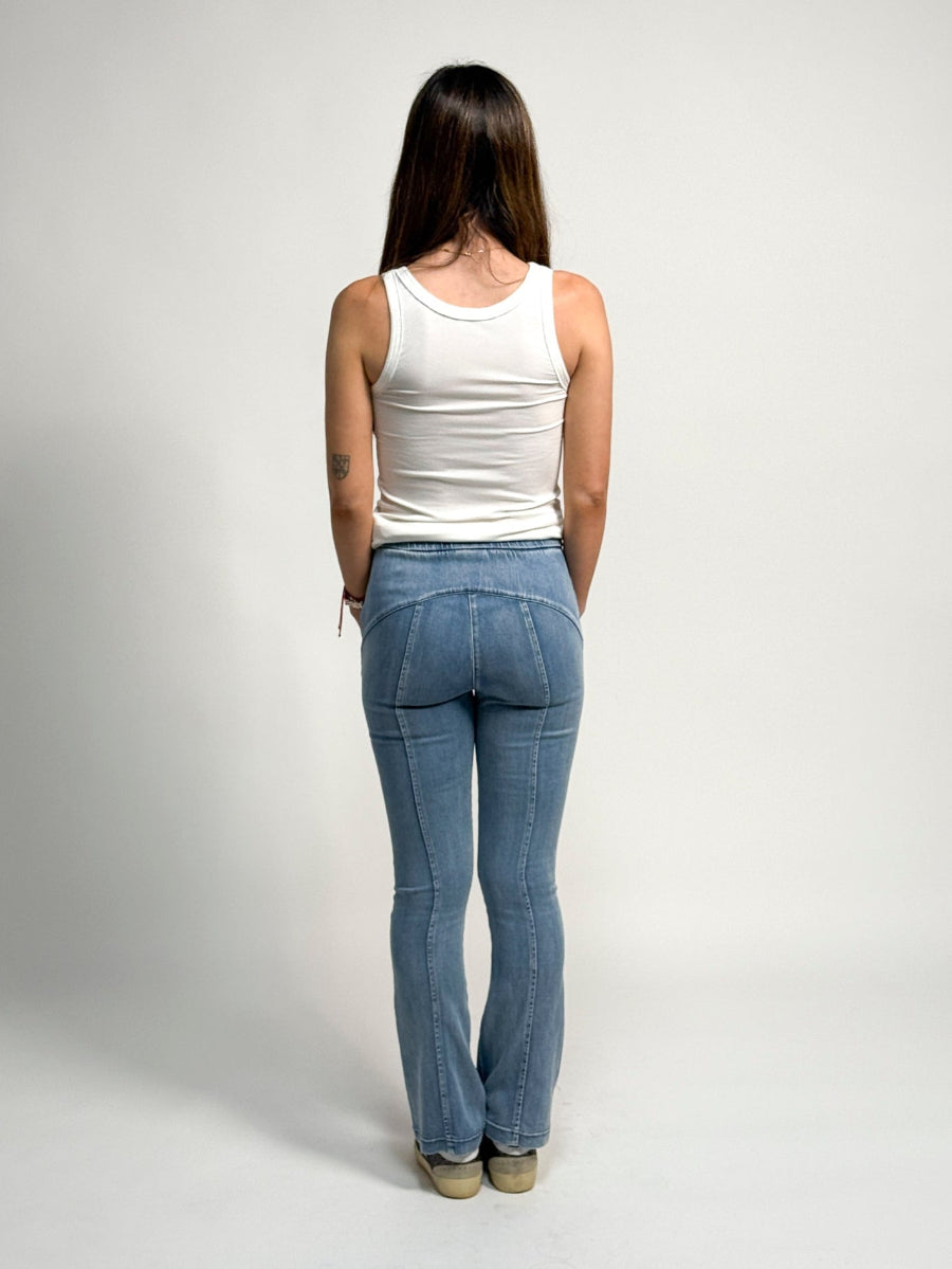 Woman wearing a white tank top and light blue water jeans by inlarkin against a plain background, from the back