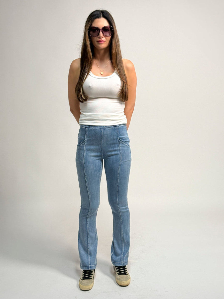 Woman wearing a white tank top and light blue water jeans by inlarkin against a plain background