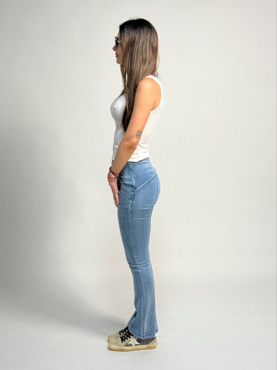 Woman wearing a white tank top and light blue water jeans by inlarkin against a plain background, side view