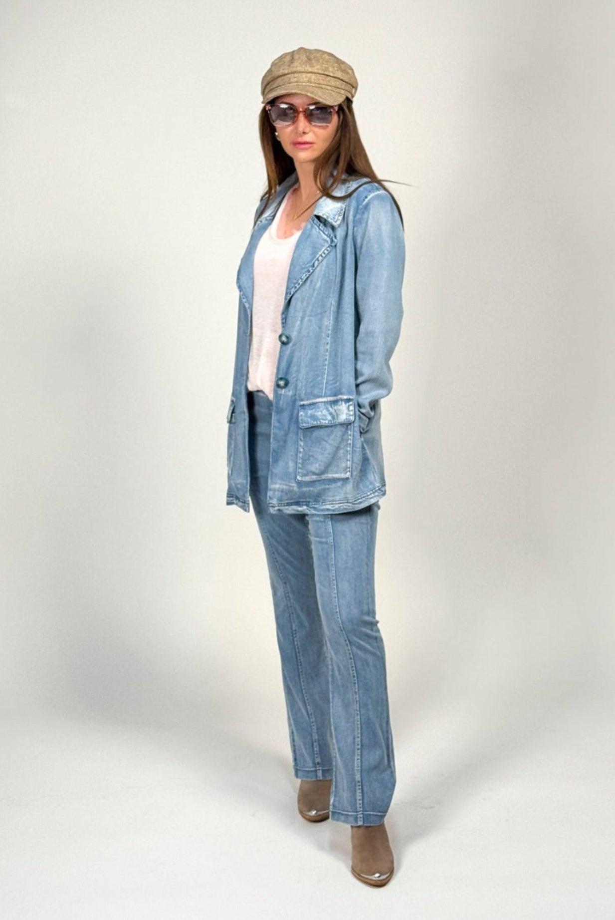 Woman wearing a blue denim jane jacket and water jean by inlarkin with a beige cap and sunglasses on a white background