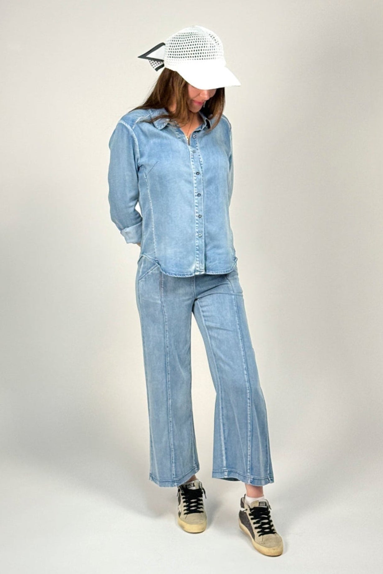 Woman wearing a denim outfit featuring the alex shirt and whitley jean by inlarkin with a white cap on a plain background