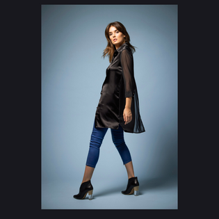  Model wearing the (UN)REAL Jean and Aliferous Shirt Dress in Black posing on a blue backdrop
