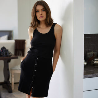  woman standing against a white wall in a contemporary beach house wearing a black variegated tank top and black button up skirt by inlarkin