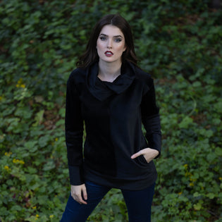  woman standing outdoors in an ivy patch wearing a black pullover cowl neck sweatshirt and dark denim jeans