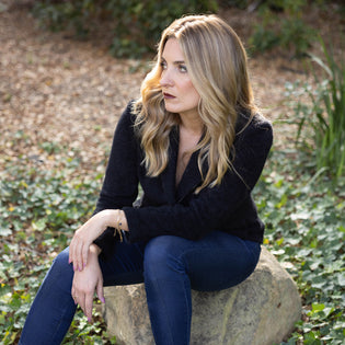  woman sitting on a rock outdoors wearing dark indigo denim jeans and a black fitted blazer with beading detail, all clothing by designer mary beth larkin and part of the metamorphous collection at inlarkin
