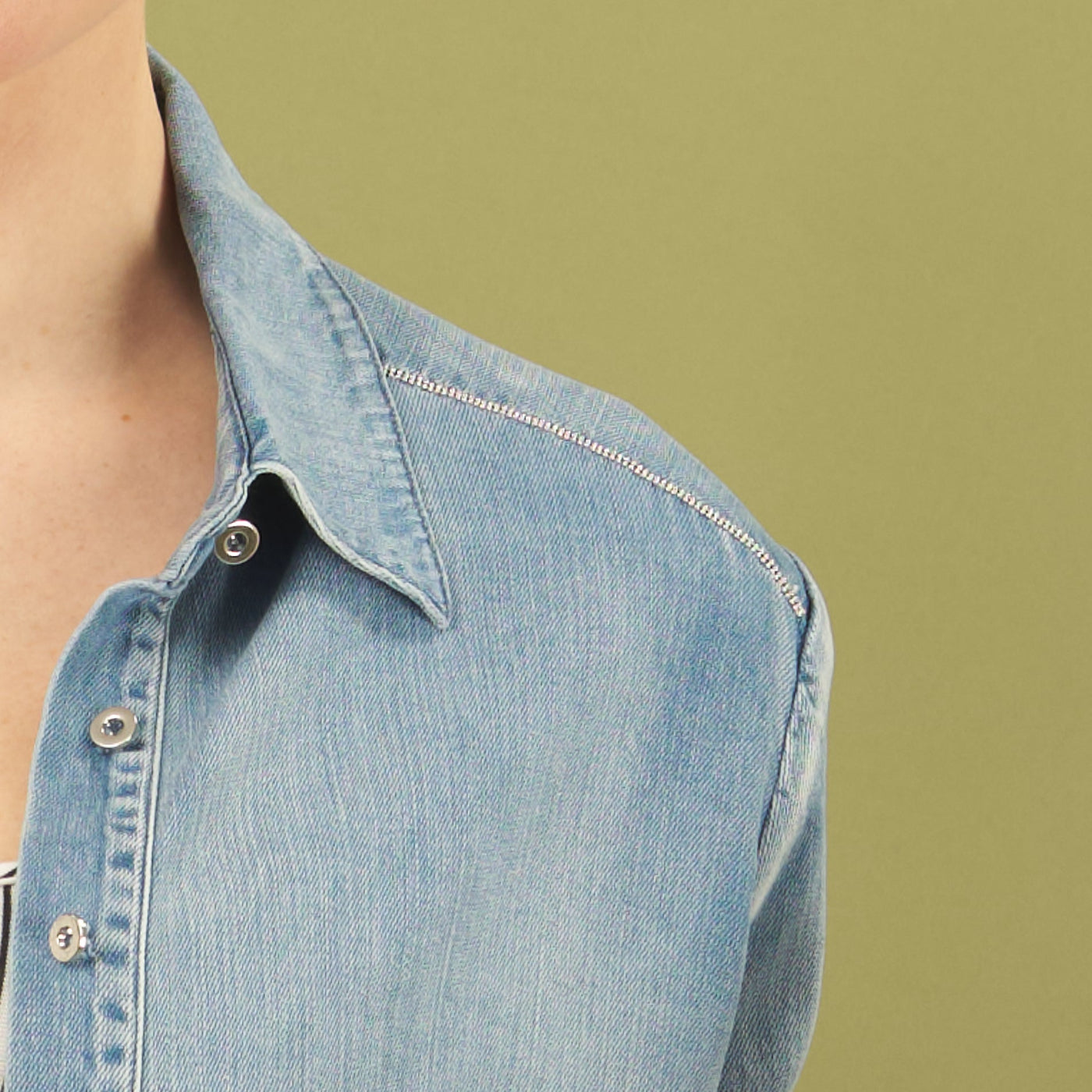 Close-up of the alex denim shirt by inlarkin with a beading on the shoulder with a green background