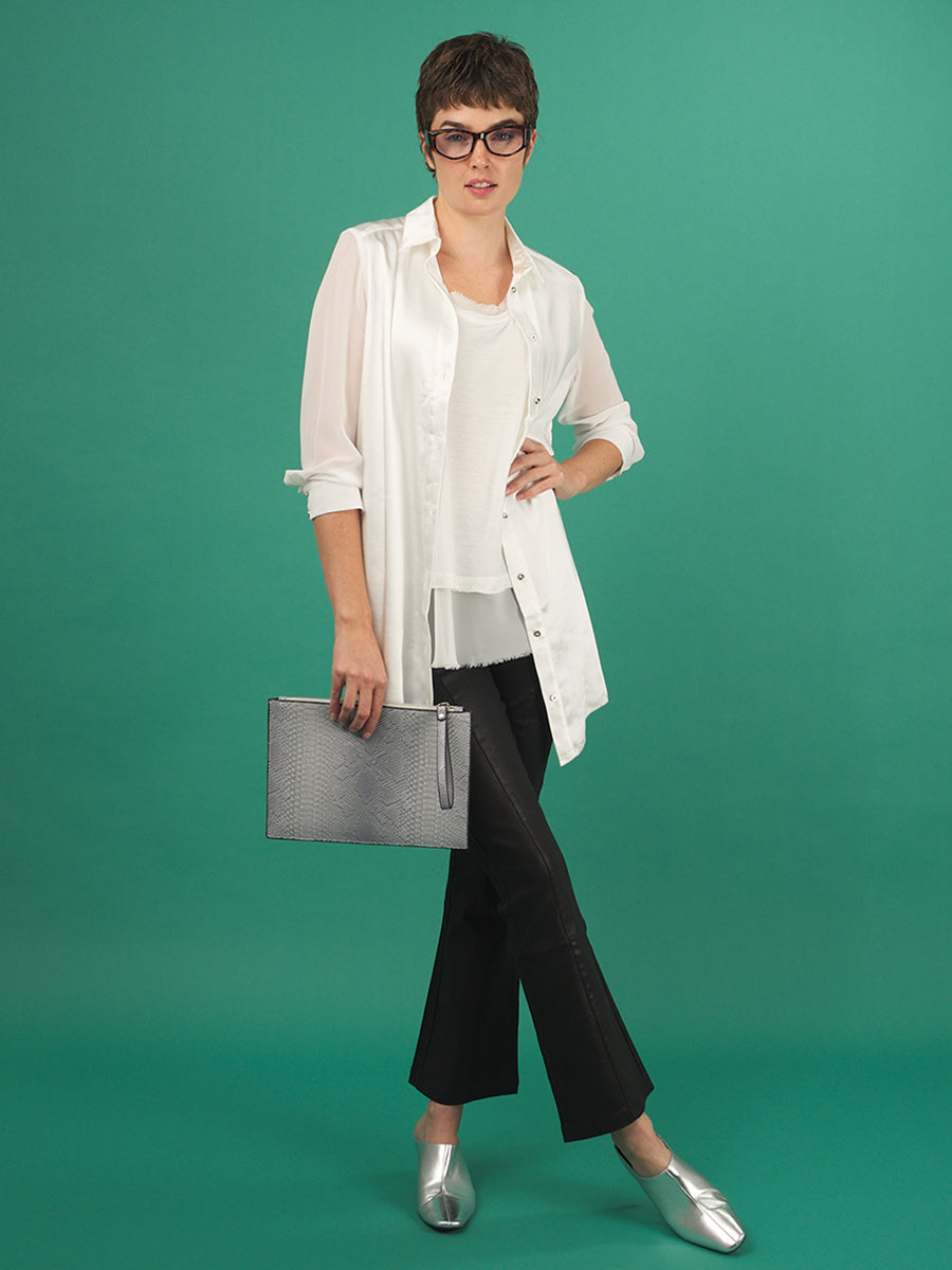 Woman holding a gray clutch, wearing a white aliferous shirtdress by inlarkin against a teal background