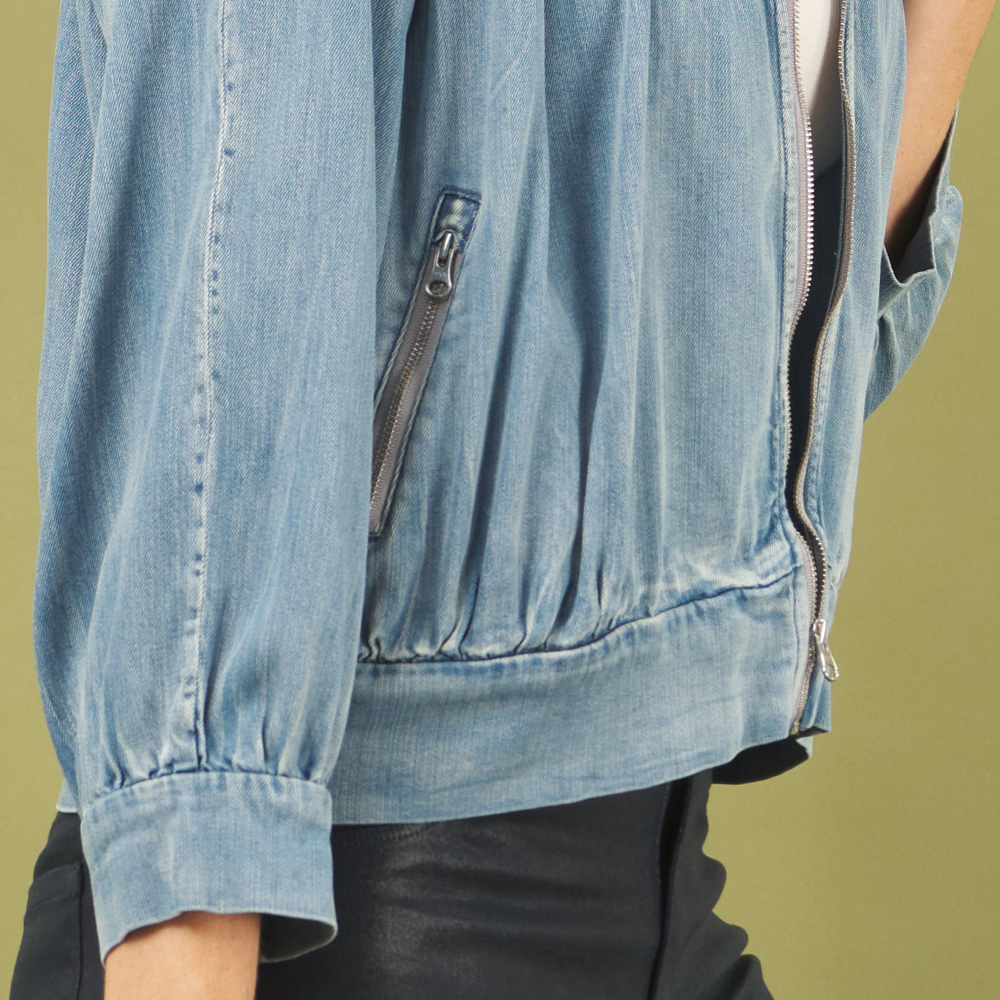 Light blue denim jacket with zippers on a green background