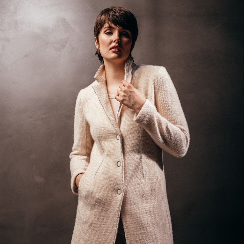  woman standing against a textured wall wearing a cream boy blazer by inlarkin showing the fabric and snap details