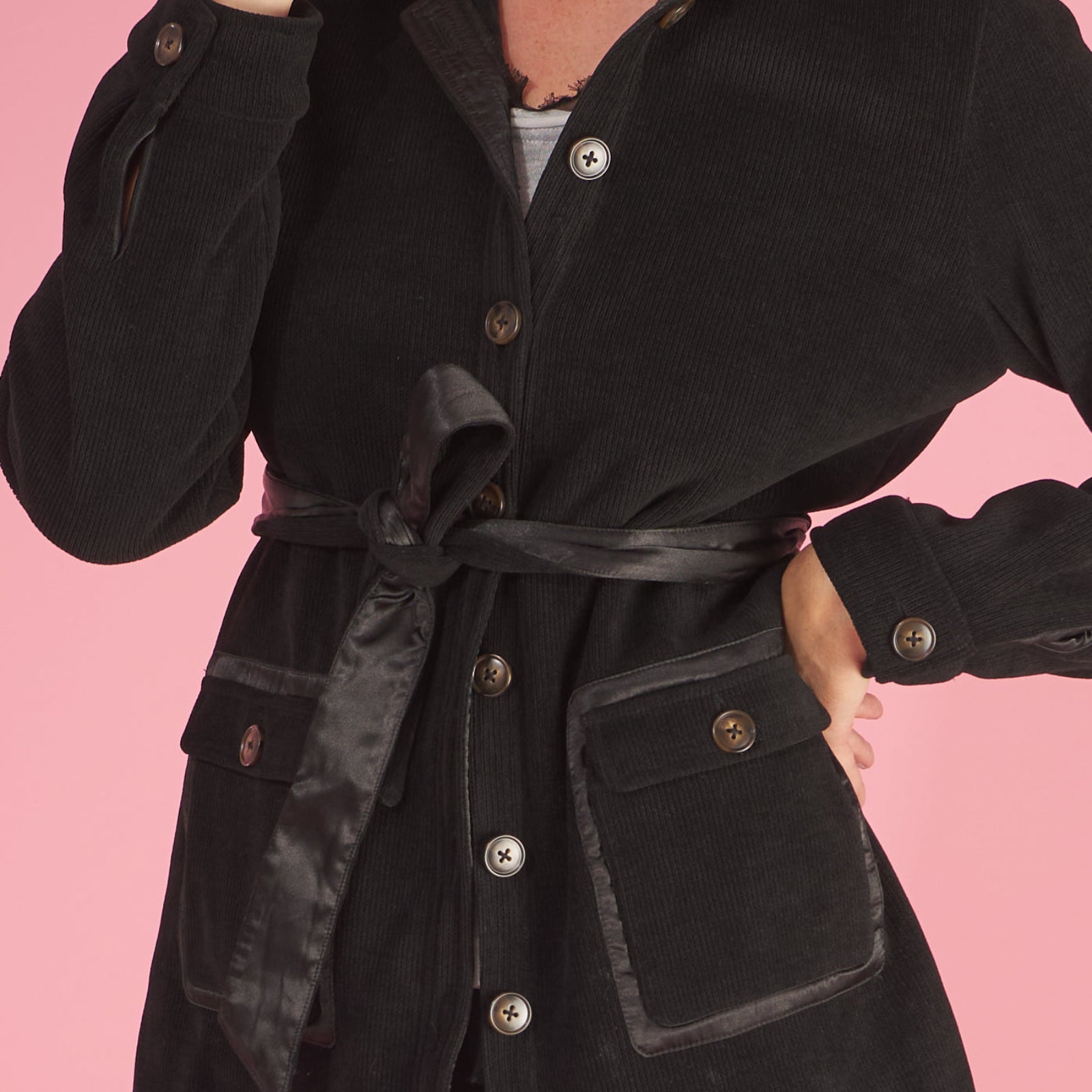 a detail of the shirt jacket by inlarkin in black showing the front profile pockets, sea glass buttons and belted sash