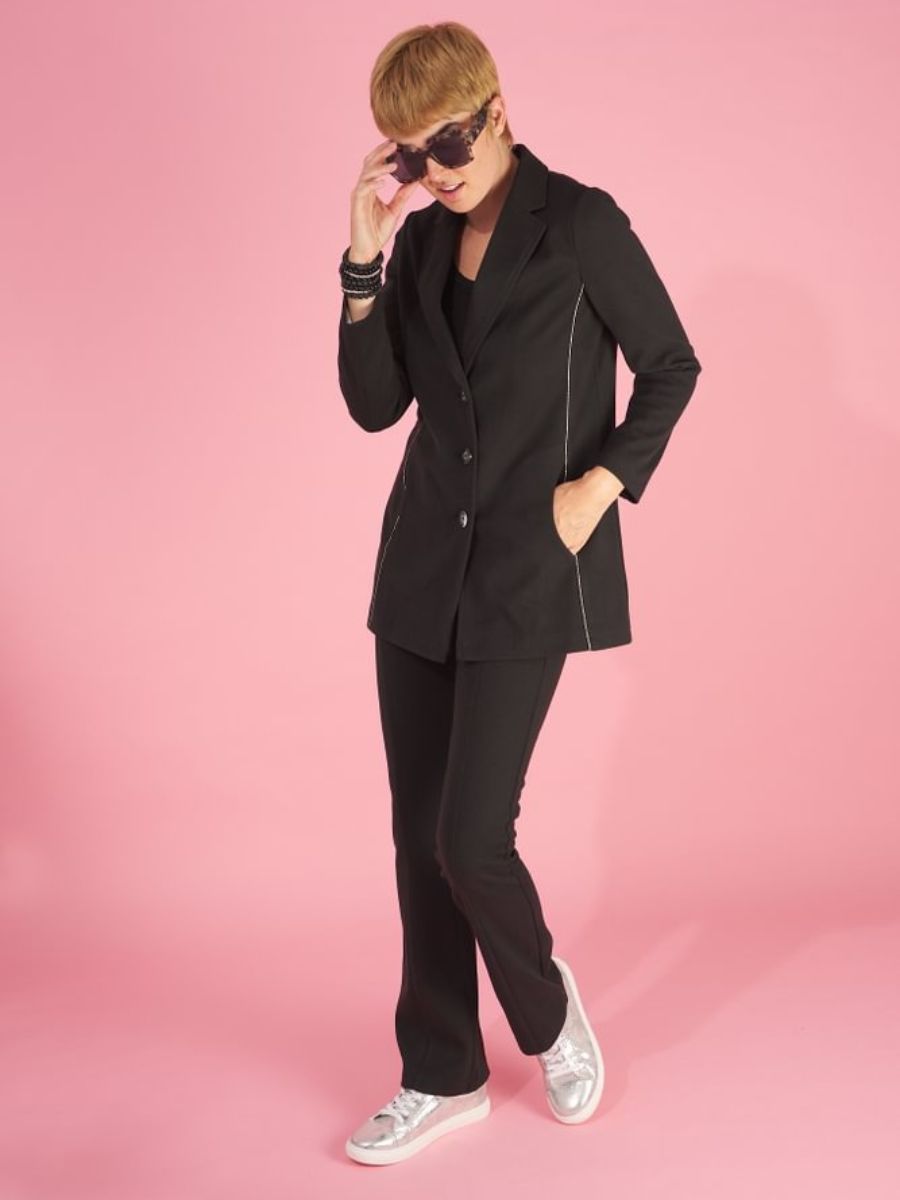 Woman wearing a black maxine blazer by inlarkin with sneakers on a pink background