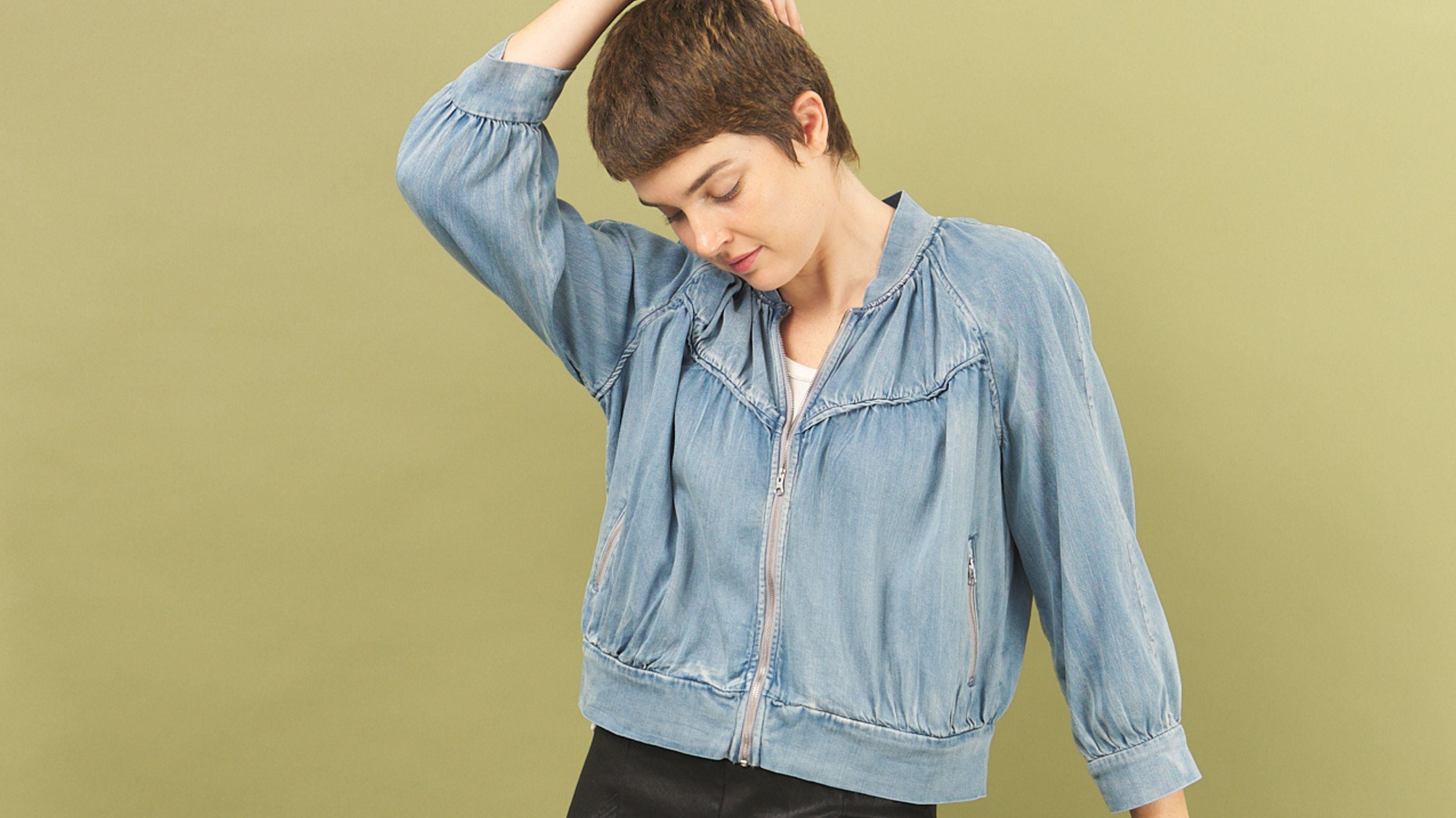 Woman wearing a light blue denim boy bomber jacket by inlarkin against a solid background