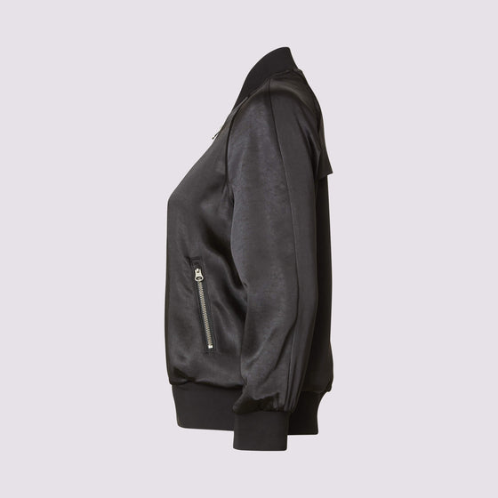 side view of the olivia beauty bomber jacket in black showing the fabric sheen, zipper detail on front and pockets and piping trim